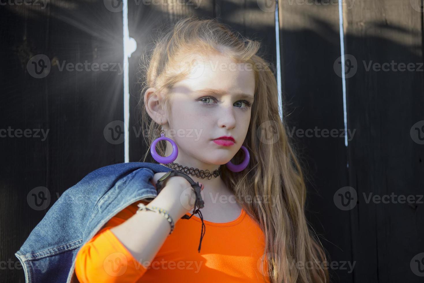 retrato do uma pequeno menina com brilhante Maquiagem em pé de uma de madeira cerca. ruivo pequeno garota. foto