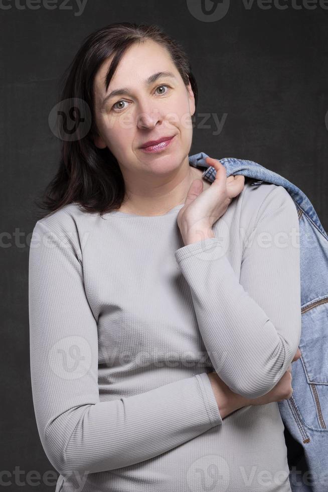 lindo cinquenta ano velho mulher com Sombrio cabelo em uma cinzento fundo. retrato do uma meia idade mulher. foto