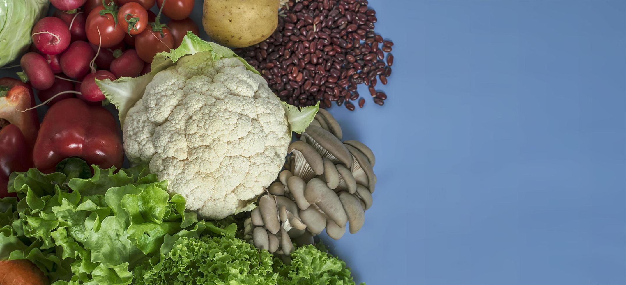 produtos para uma dieta desintoxicante vegetariana de couve-flor, alface, rabanete, tomate, cogumelos, feijão e pimentão vermelho sobre fundo azul foto