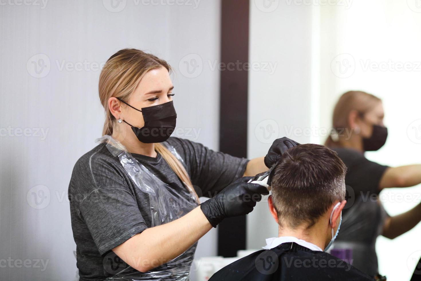 uma cabeleireiro com segurança medidas para COVID-19, cortes uma homem dentro uma remédio mascarar, social distância, corte cabelo com uma médico mascarar e luvas. foto