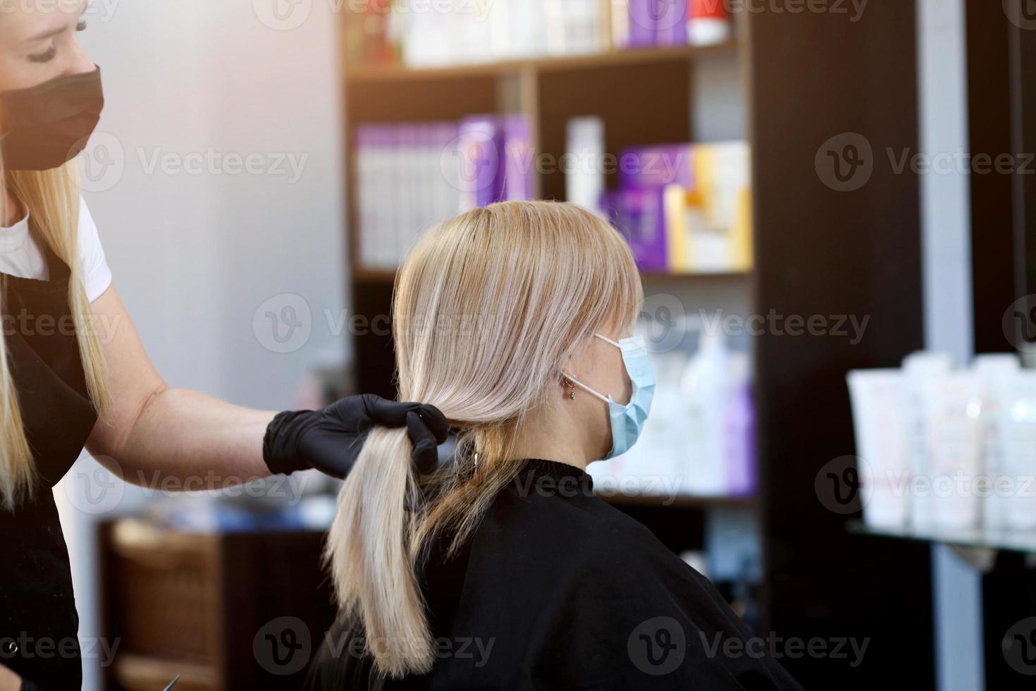 cabeleireiro com segurança medidas para COVID-19, uma mulher dentro uma médico mascarar, social distância, corte cabelo com uma médico mascarar e borracha luvas dentro uma beleza salão. foto
