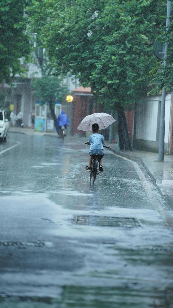 Guangzhou cidade, China, 2022 - 1 Garoto equitação a bicicleta através a rua dentro a chuvoso dia foto