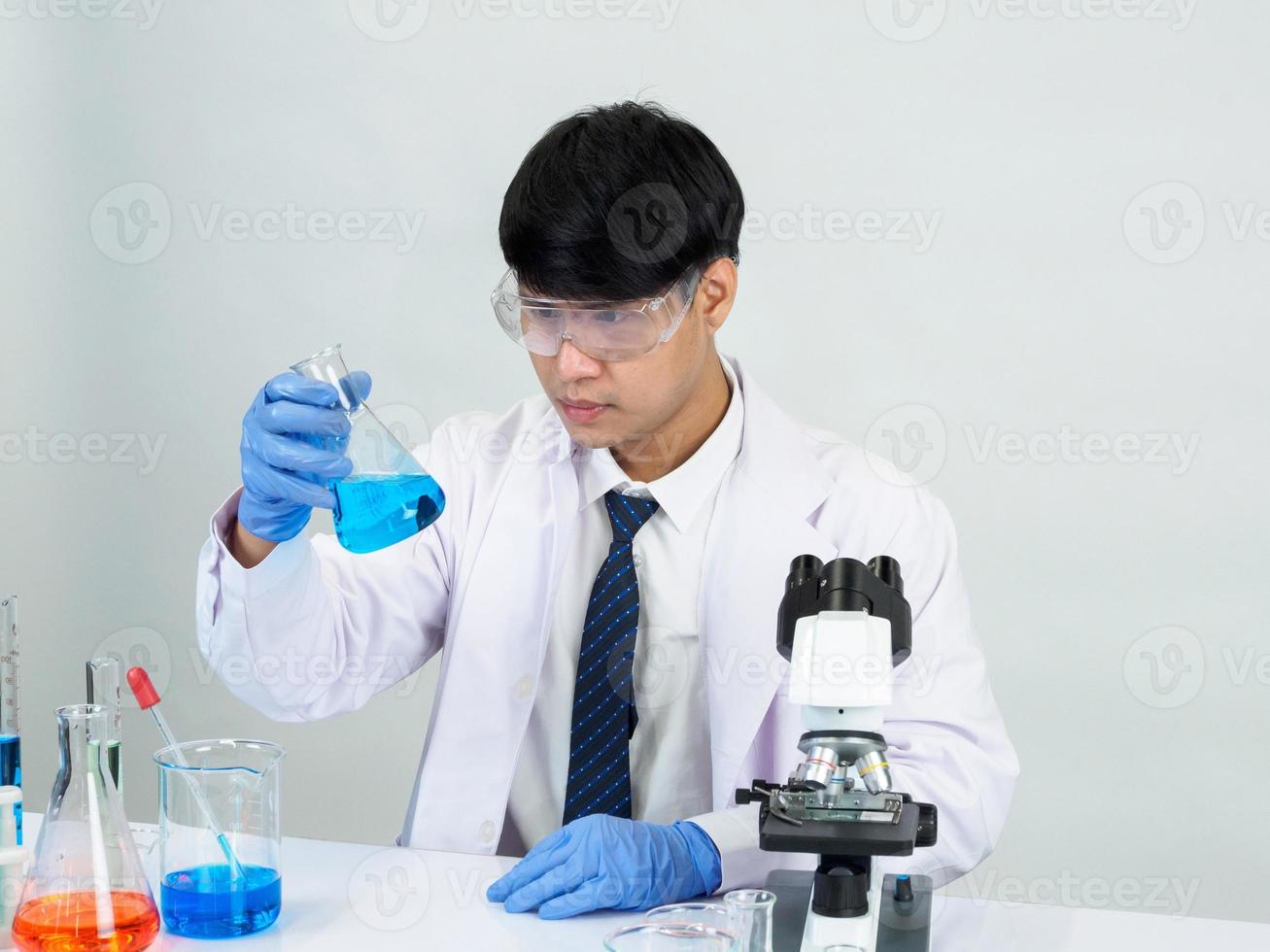 cientista estudante asiático no laboratório de mistura de reagentes em um laboratório de pesquisa científica com tubos de ensaio de vários tamanhos e microscópios. em cima da mesa no fundo branco do laboratório de química de laboratório. foto