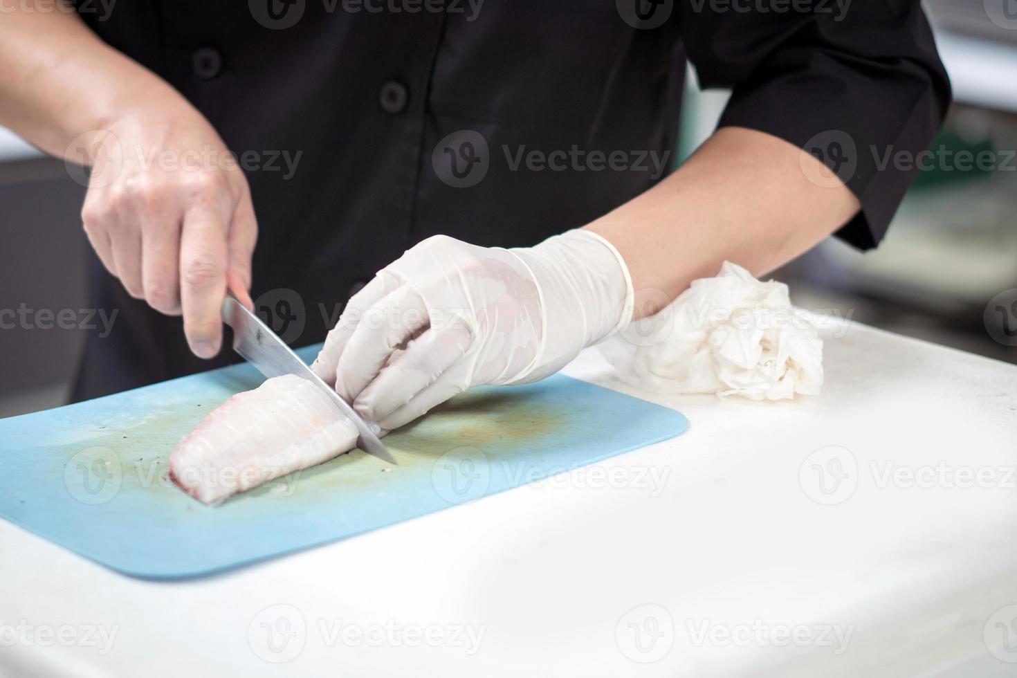focado masculino chefe de cozinha dentro uniforme corte peixe filé em quadro, chefe de cozinha cortes branco tilápia peixe dentro cozinha. foto