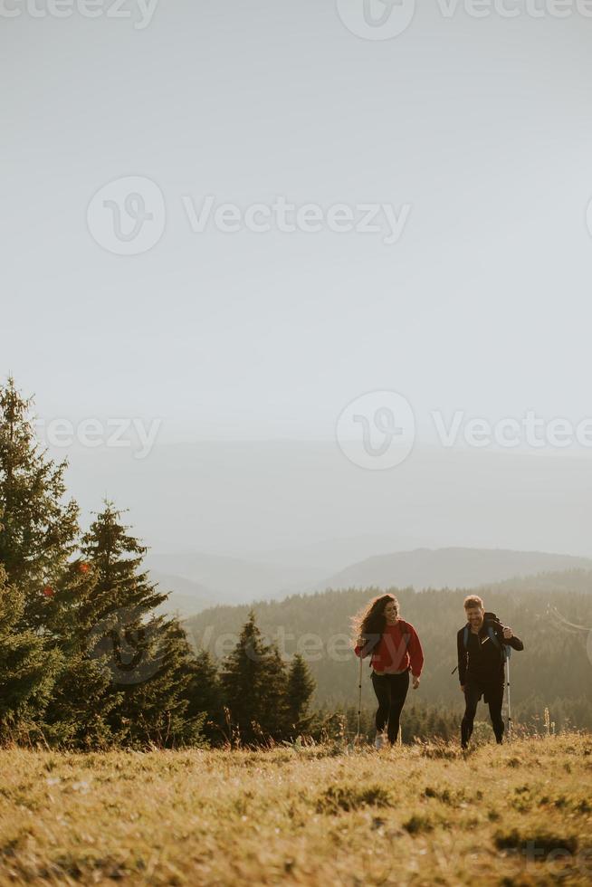 casal sorridente caminhando com mochilas pelas colinas verdes foto