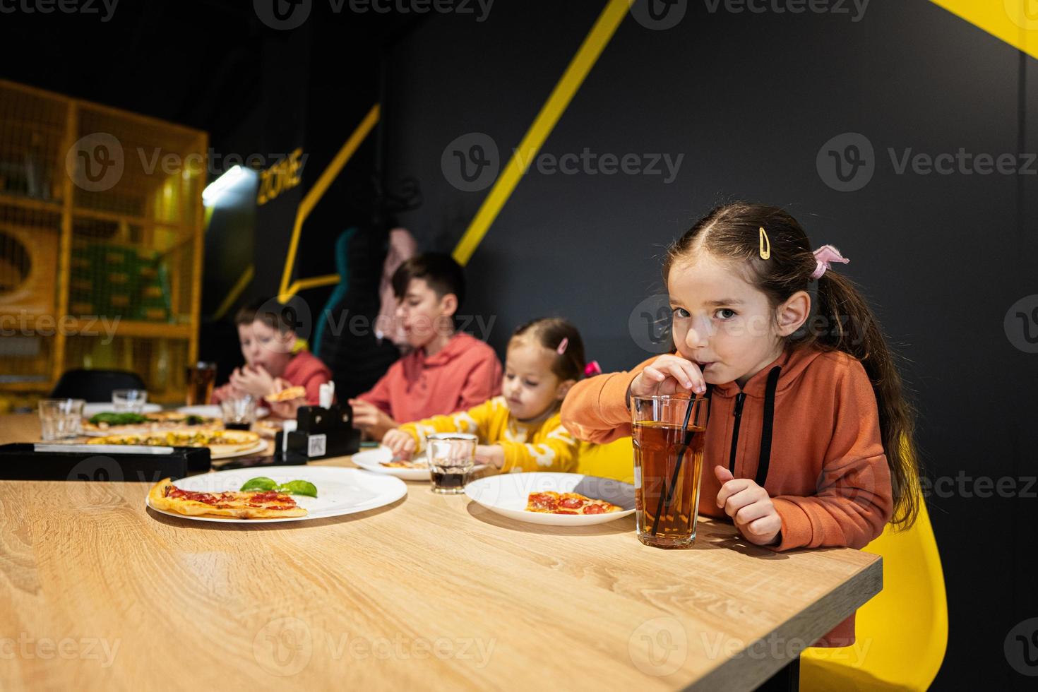 quatro crianças comendo italiano pizza dentro pizzaria. crianças comer às cafeteria. menina beber suco. foto