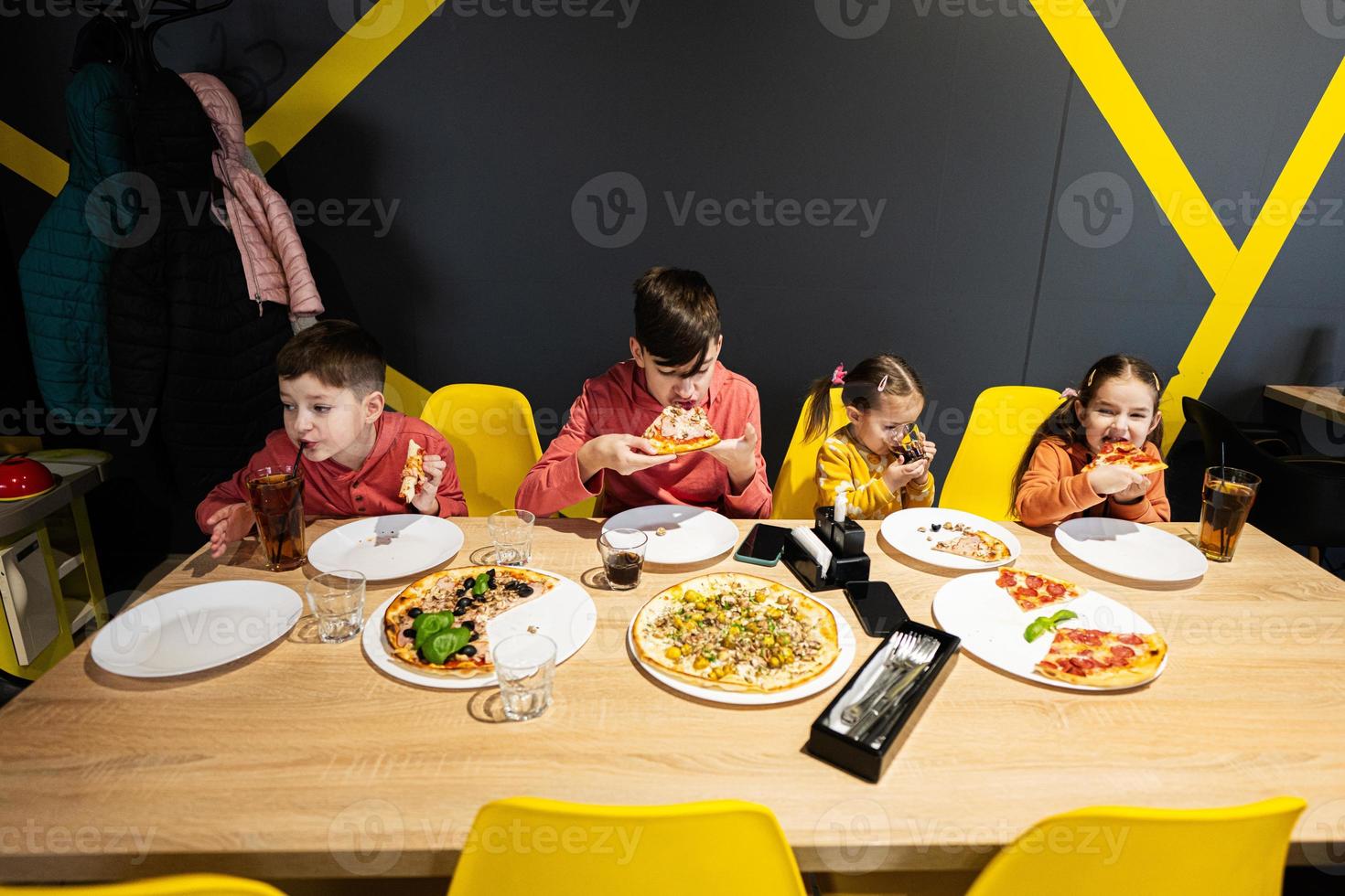 quatro crianças comendo italiano pizza dentro pizzaria. crianças comer às cafeteria. foto