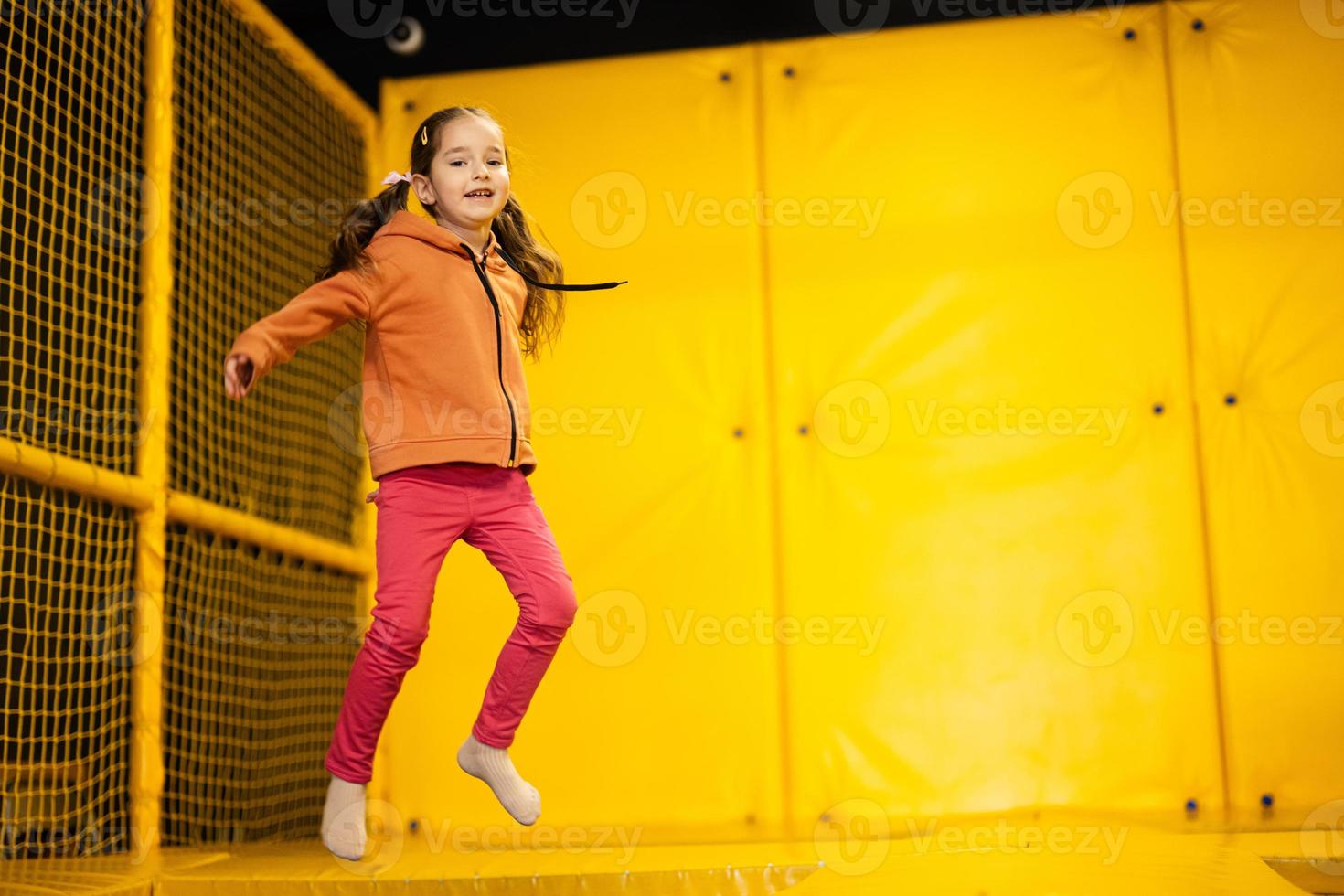 pequeno menina criança pulando em trampolim às amarelo Parque infantil parque. criança dentro movimento durante ativo entretenimento. foto