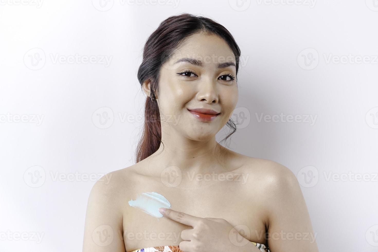 pele Cuidado produtos conceito. ásia mulher aplicando hidratante loção em corpo depois de banho, em pé embrulhado dentro toalha, cortada imagem foto