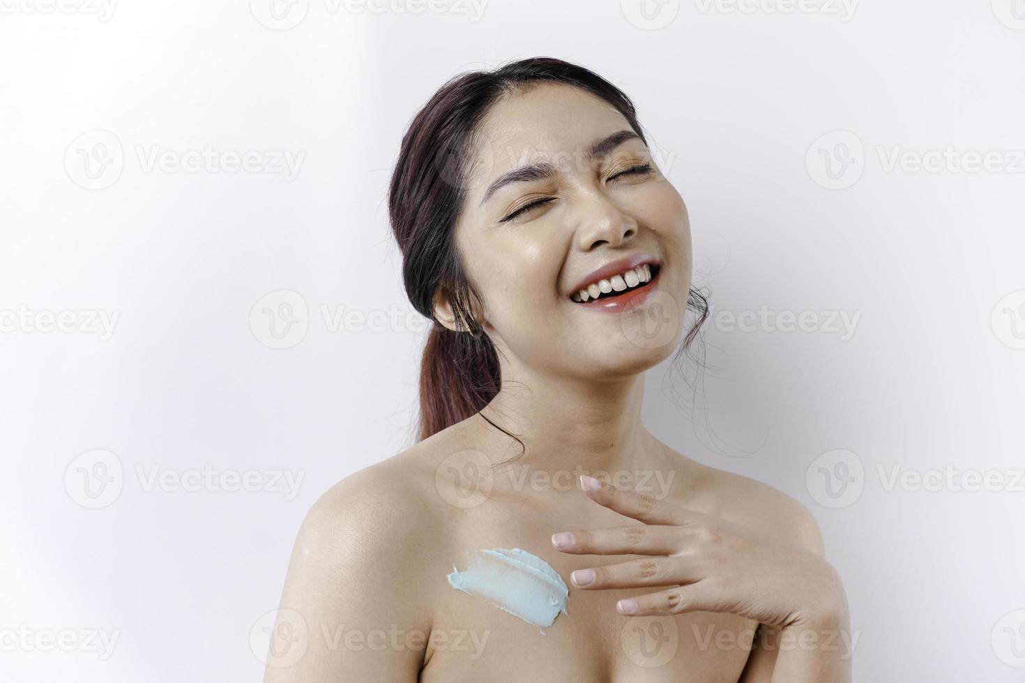 pele Cuidado produtos conceito. ásia mulher aplicando hidratante loção em corpo depois de banho, em pé embrulhado dentro toalha, cortada imagem foto