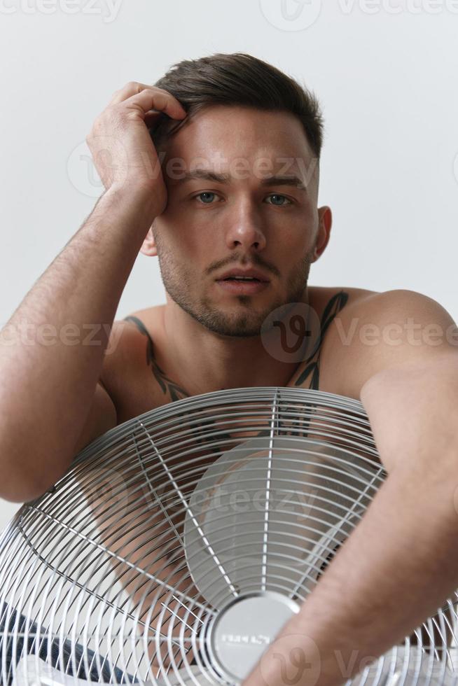 modelagem instantâneos. fechar-se retrato do atraente nu bonito homem dentro jeans inclinado em ventilador sentado em chão posando dentro branco estúdio fundo. moda homens tiro conceito. cópia de espaço. legal oferta foto