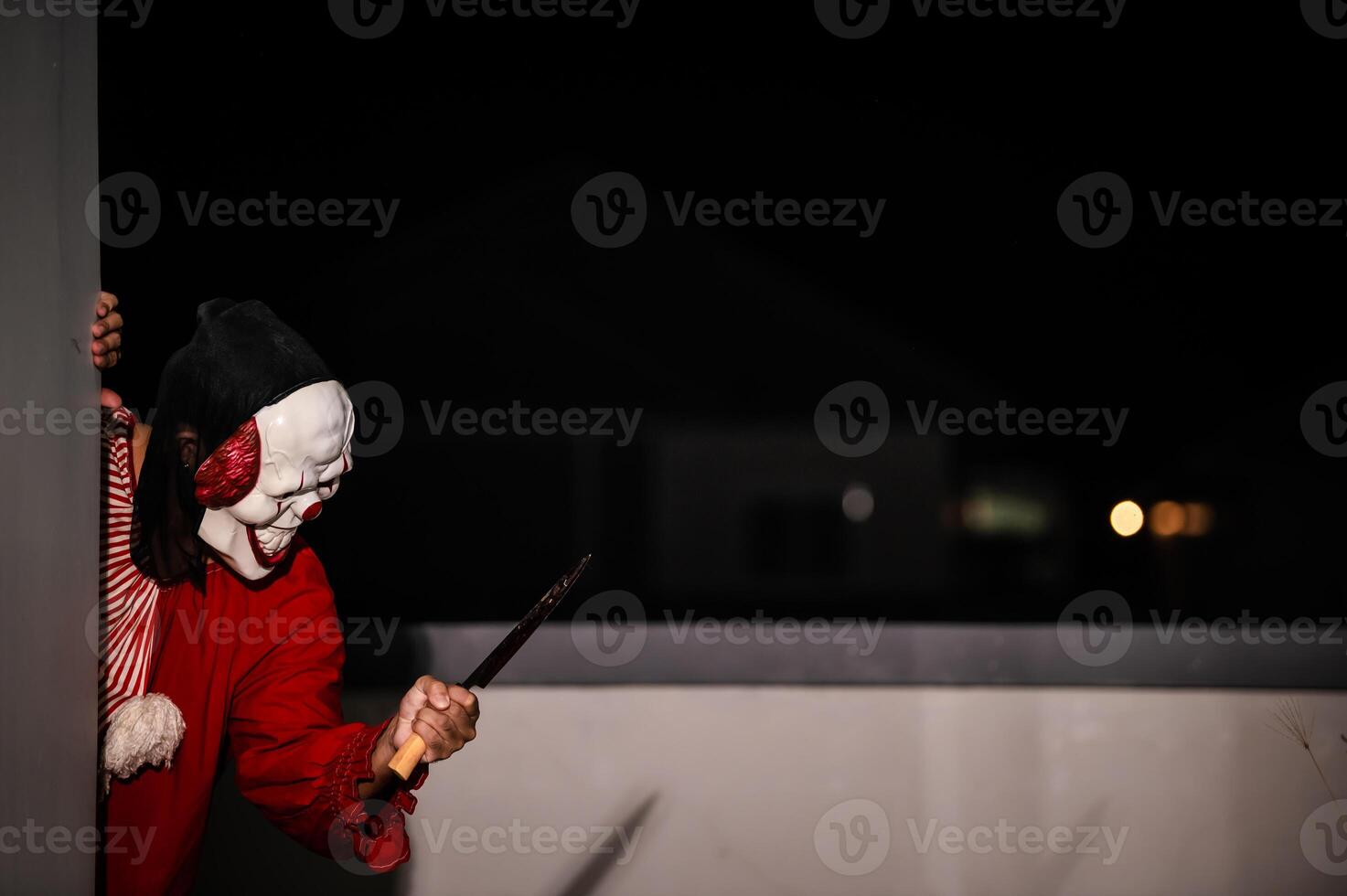 ásia bonito homem vestem palhaço mascarar com arma às a noite cena, dia das bruxas festival conceito, horror assustador foto do uma assassino dentro laranja pano, mal palhaço personagem