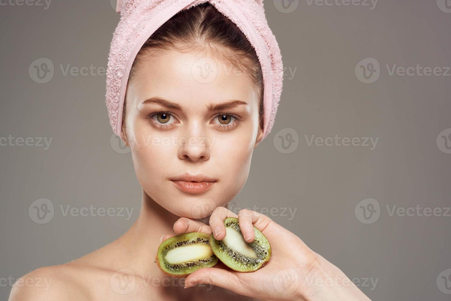 mulher com Rosa toalha em dela cabeça nu ombros cortada Visão do kiwi fruta dentro saúde mão foto