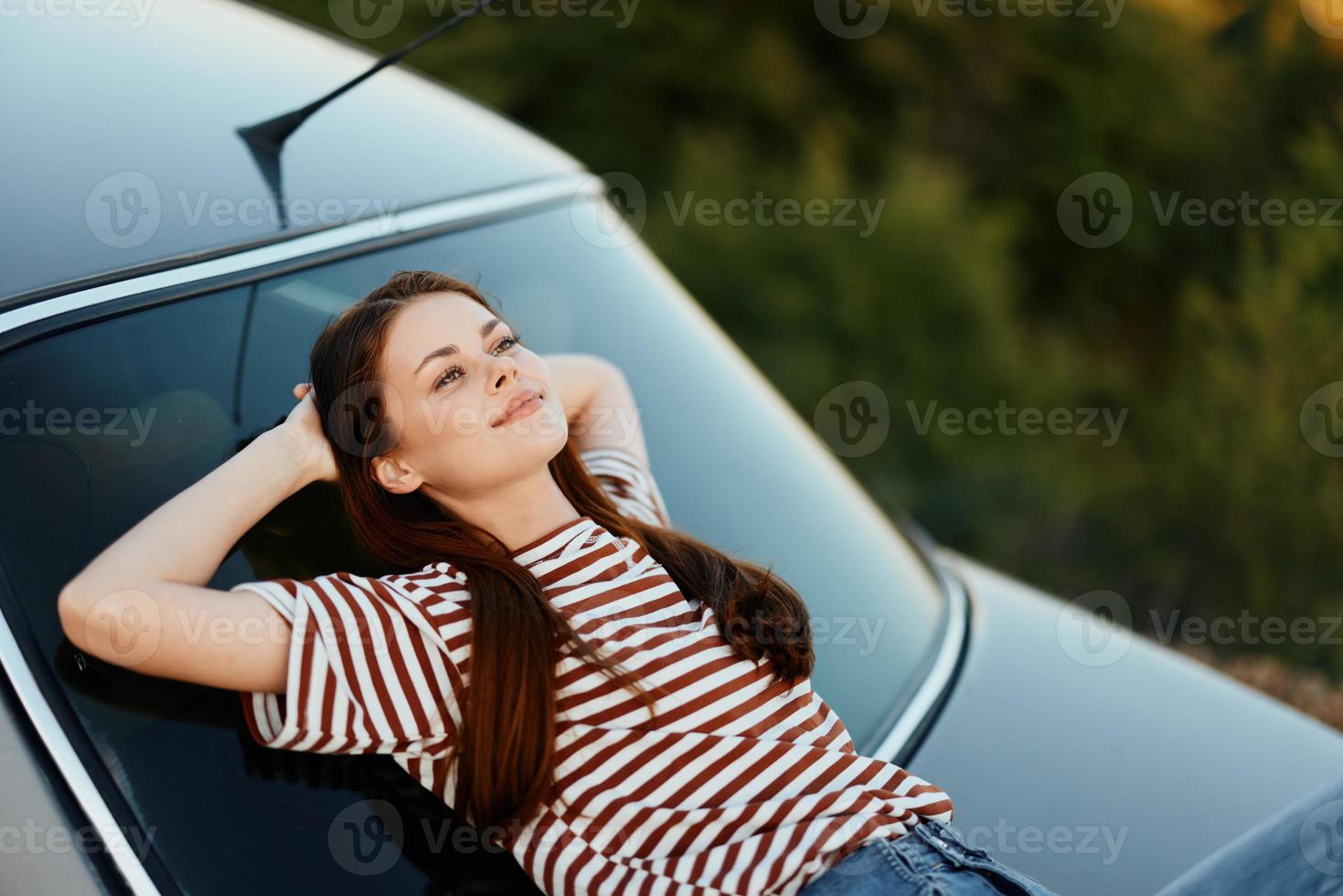 a mulher motorista parado em a estrada e deitar baixa em a carro para descansar e Veja às a lindo panorama dentro uma listrado camiseta e jeans. complicado viagem para natureza foto