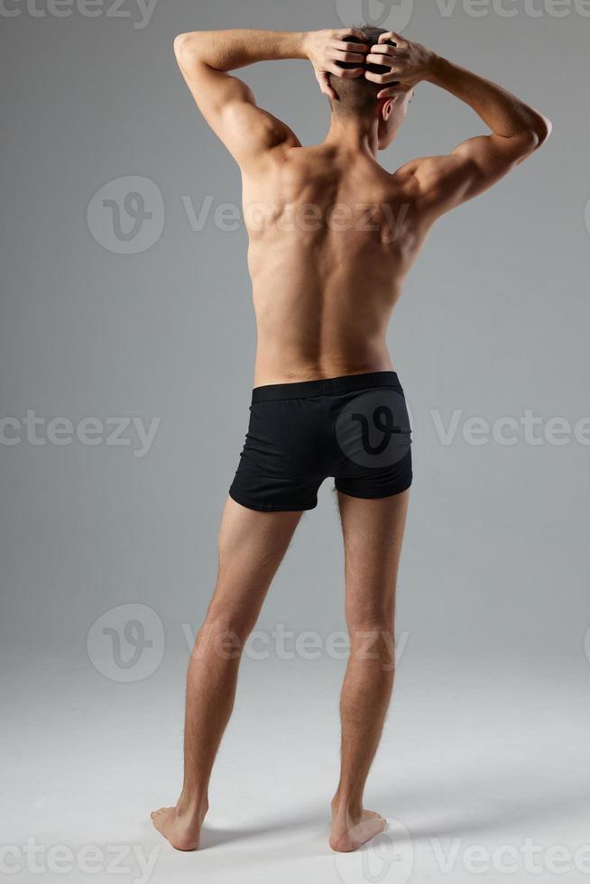 desportivo homem dentro Preto calção detém mão em cabeça costas Visão exercite-se ginástica foto