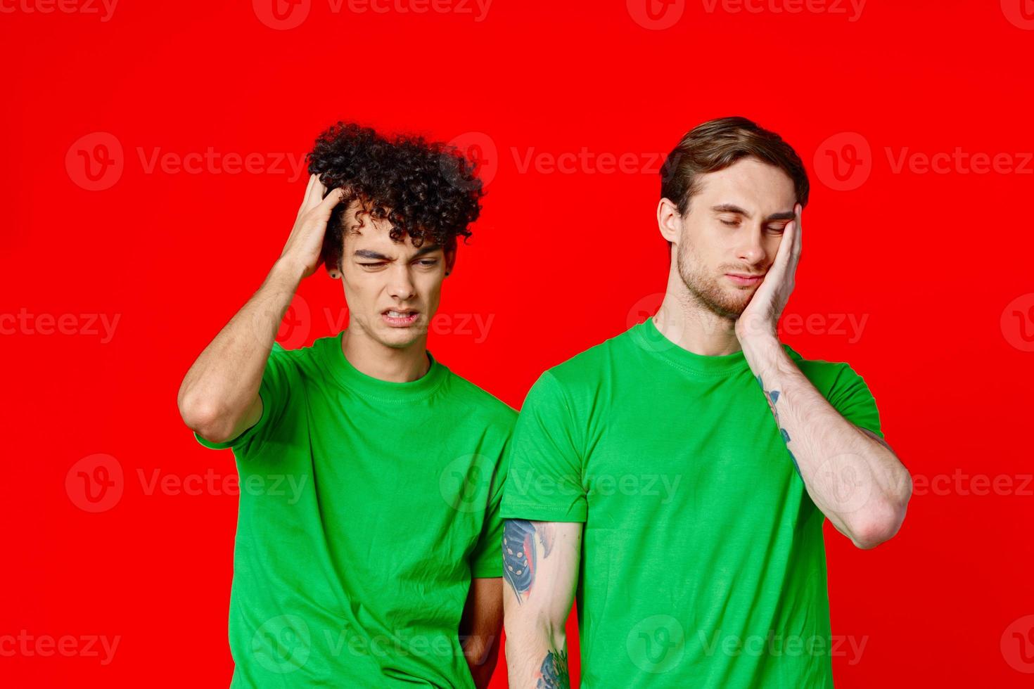 dois homens segurando seus cabeças dentro verde Camisetas em uma vermelho fundo foto