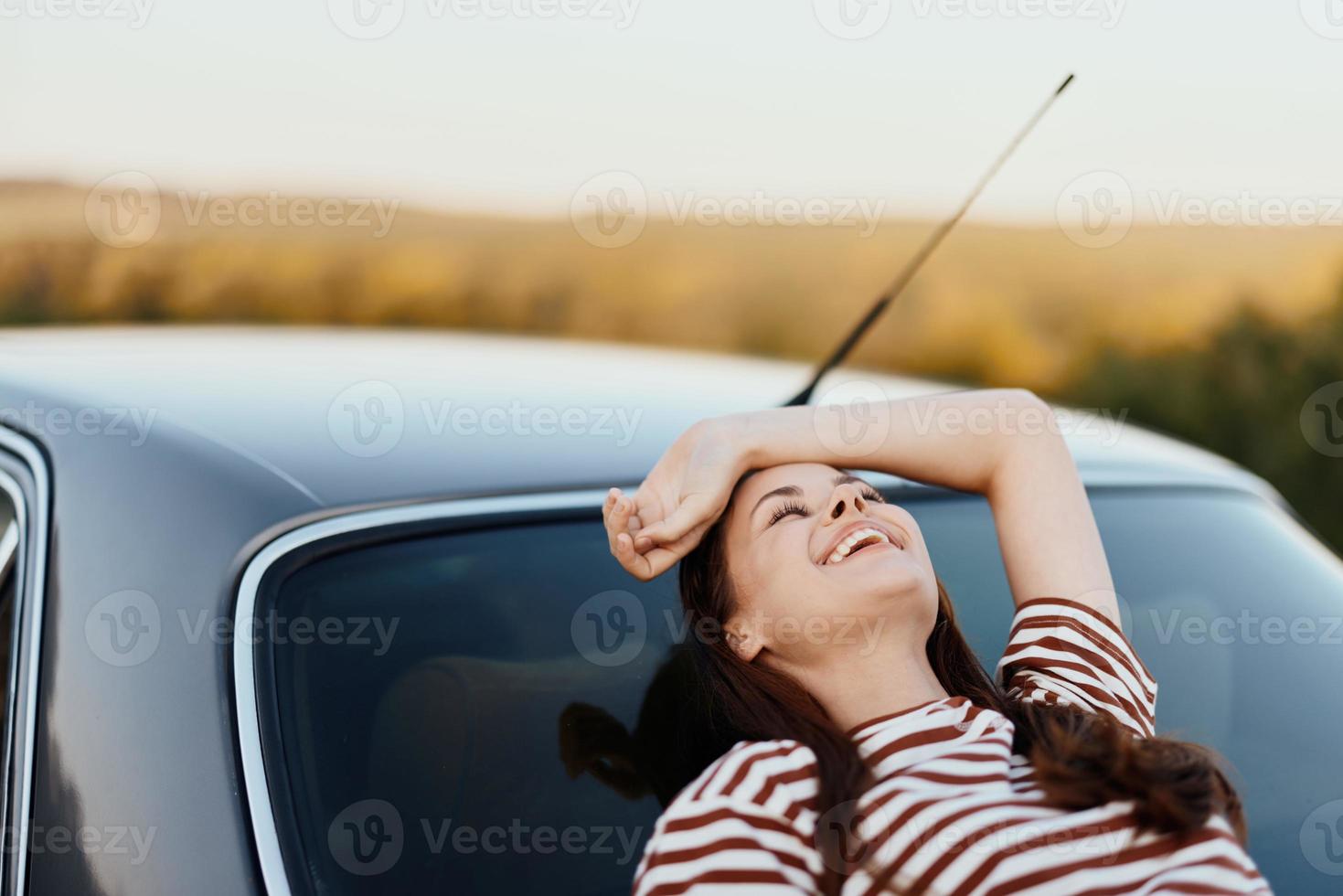 a mulher motorista parado em a estrada e deitar baixa em a carro para descansar e Veja às a lindo panorama dentro uma listrado camiseta e jeans. complicado viagem para natureza foto