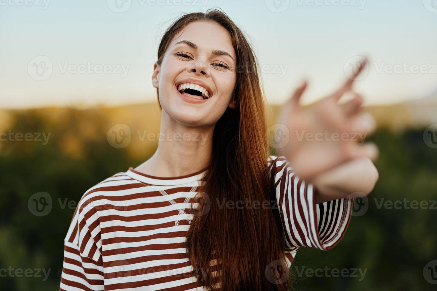 mulher sorridente enquanto olhando às a Câmera e puxar dela mãos para a Câmera fechar-se dentro natureza com uma Visão do a montanhas. feliz viagem estilo de vida Segue mim foto