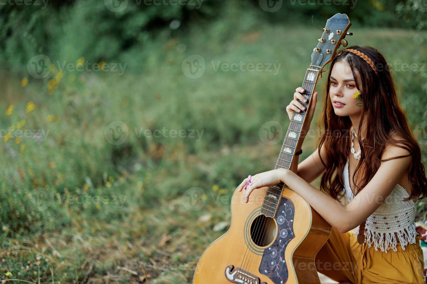 feliz hippie mulher com uma guitarra relaxante dentro natureza sentado em uma xadrez sorridente e desfrutando a visualizar. estilo de vida dentro harmonia com natureza e auto foto