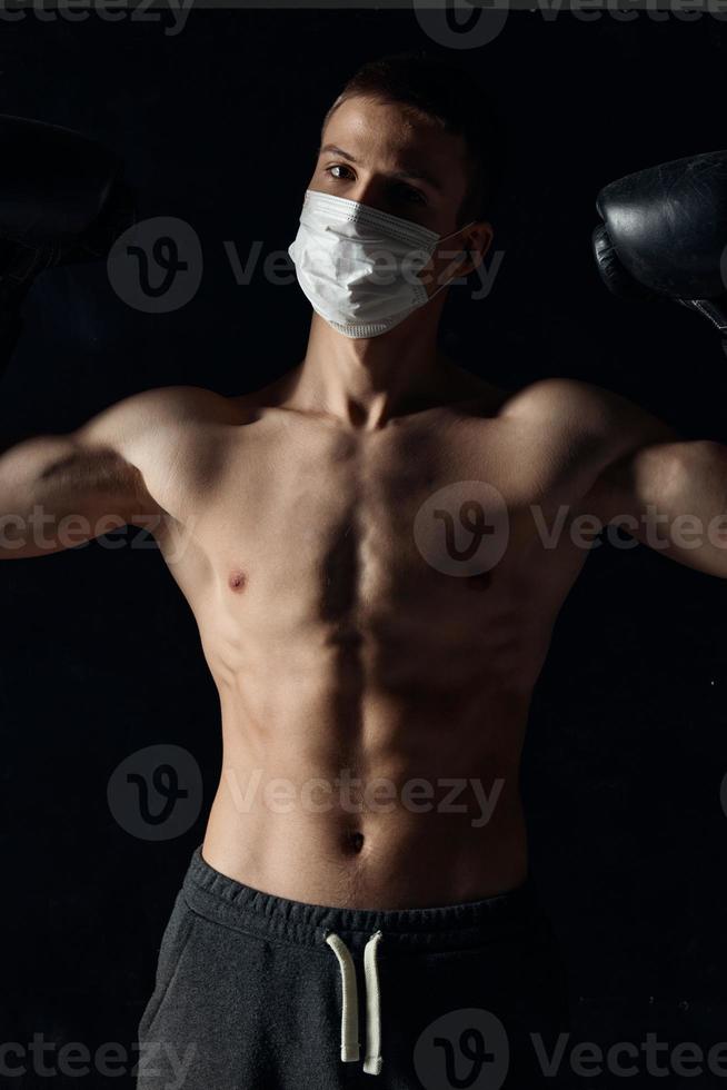 atleta dentro uma médico mascarar e boxe luvas em uma Preto fundo bombeado acima tronco foto