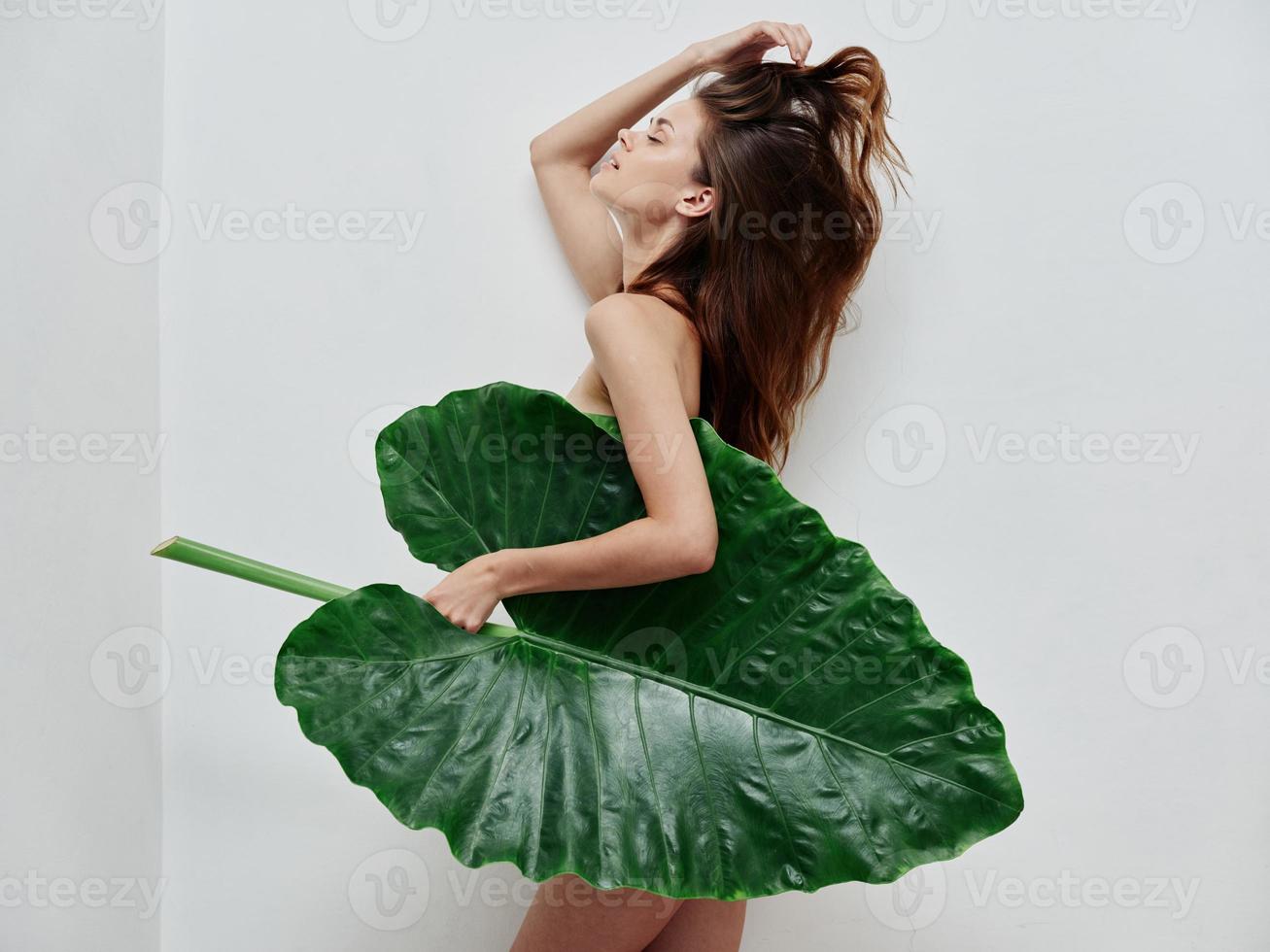 mulher segurando uma ampla verde folha dentro dela mãos nu corpo luz fundo foto