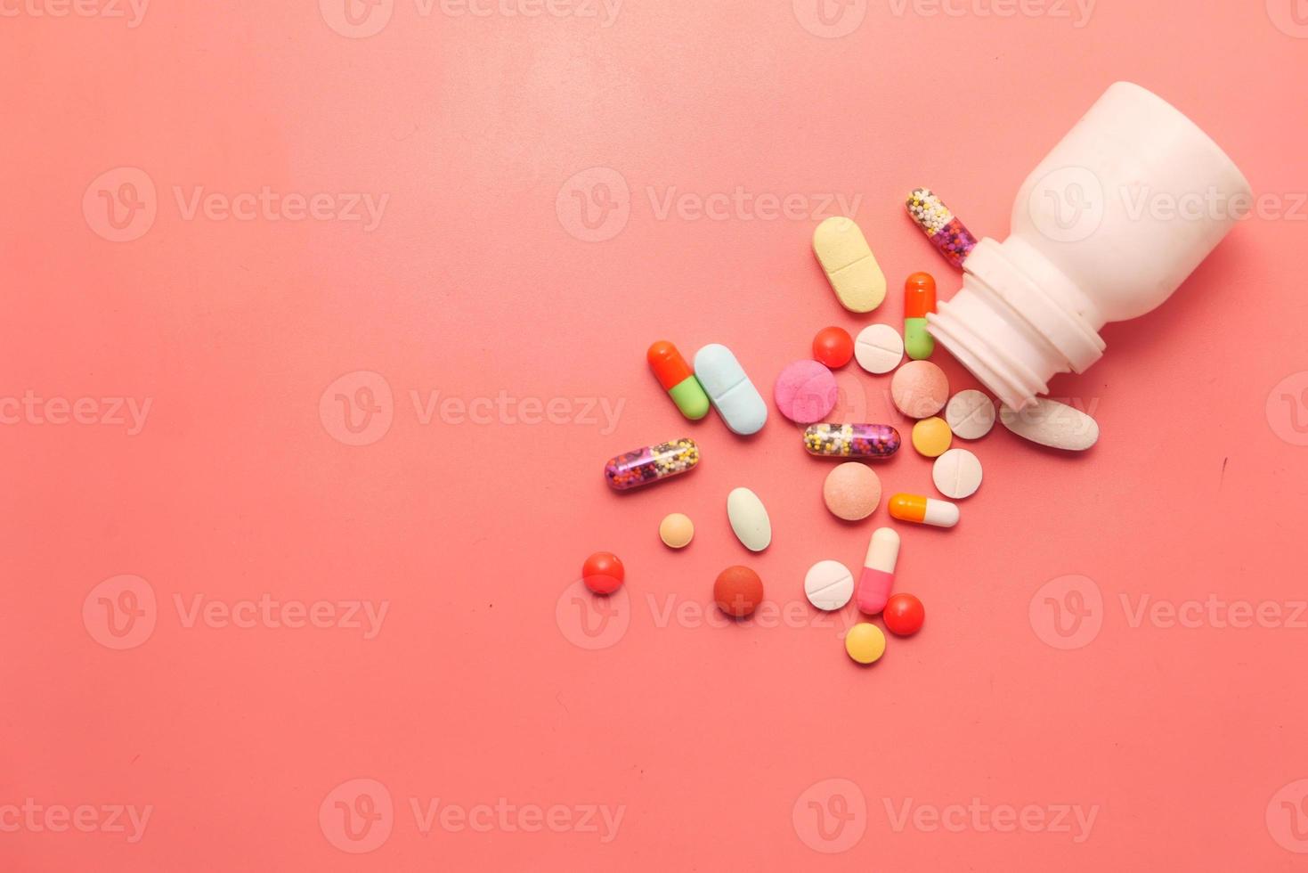 comprimidos e cápsulas derramando no fundo rosa foto