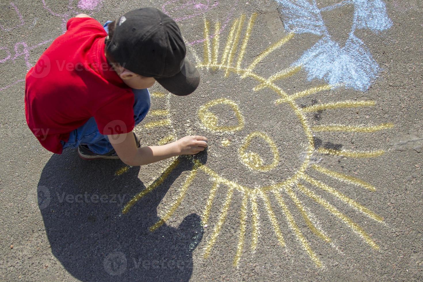 a Garoto desenha com giz em a calçada a sol.infantil rua arte. futuro artista. pequeno picaksso. foto