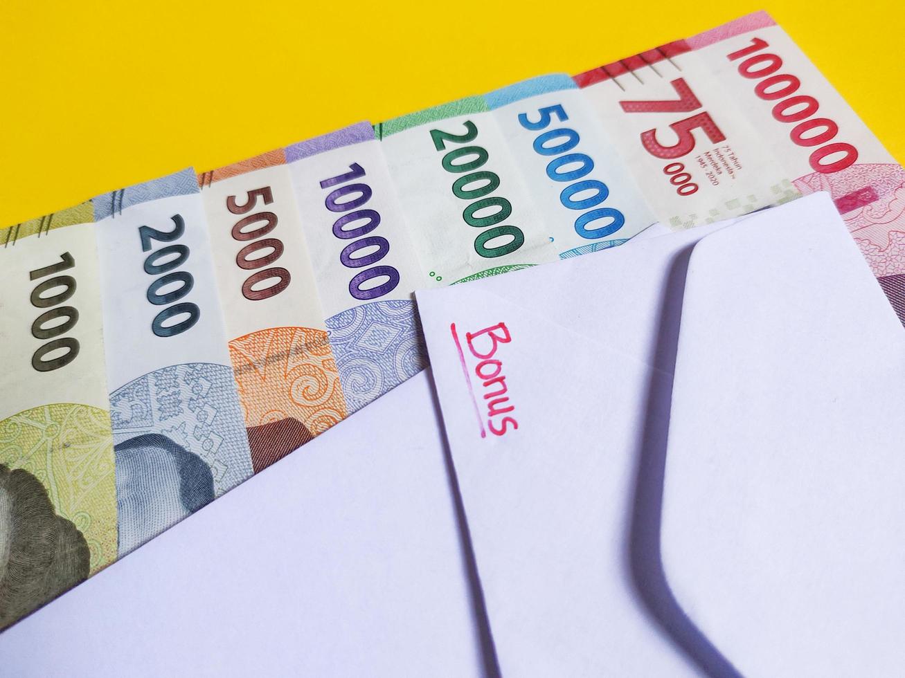 Novo notas emitido dentro 2022 a partir de Rp.1.000 para 100.000 rp. indonésio rupia moeda com uma branco envelope etiquetado bônus. Tunjangan hari raya conceito isolado em amarelo fundo foto