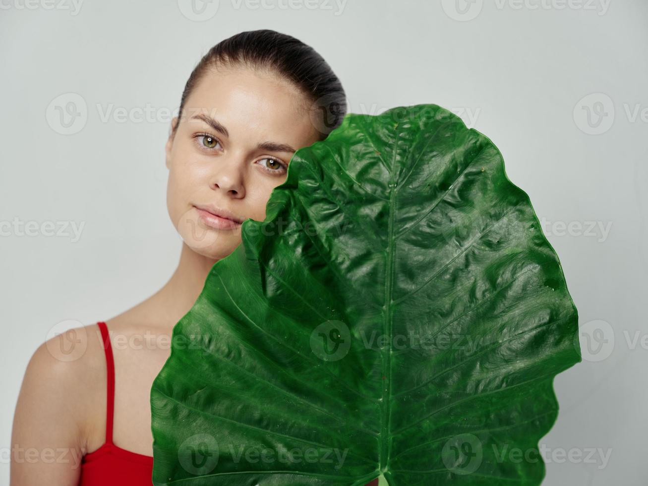 jovem mulher dentro vermelho camiseta em luz fundo com verde folha do Palma árvore cortada Visão foto