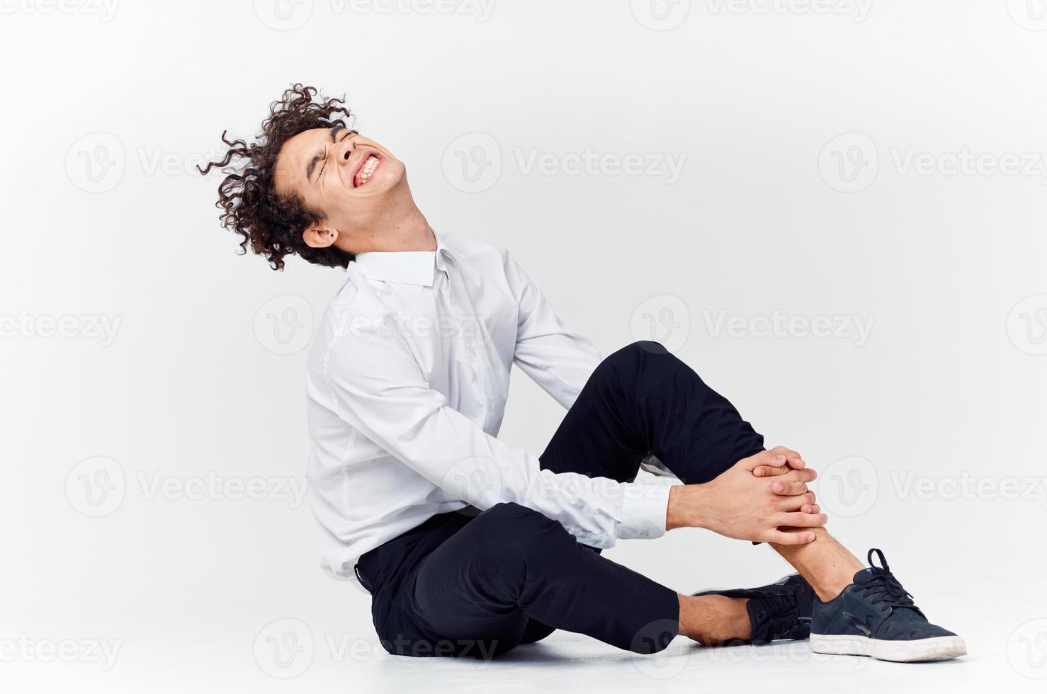 homem com encaracolado cabelo dentro uma clássico terno e tênis senta em a chão e lado Visão cópia de espaço foto