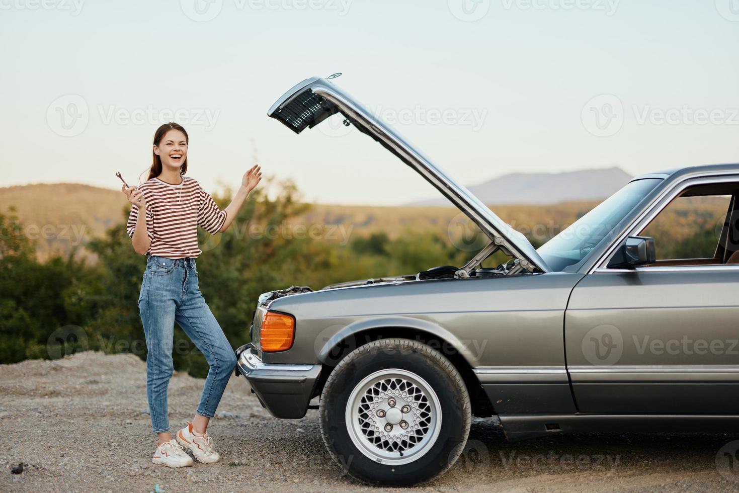 uma mulher carrinhos lado de fora uma quebrado, perigoso velho carro com uma chave inglesa em a estrada viajando sozinho foto