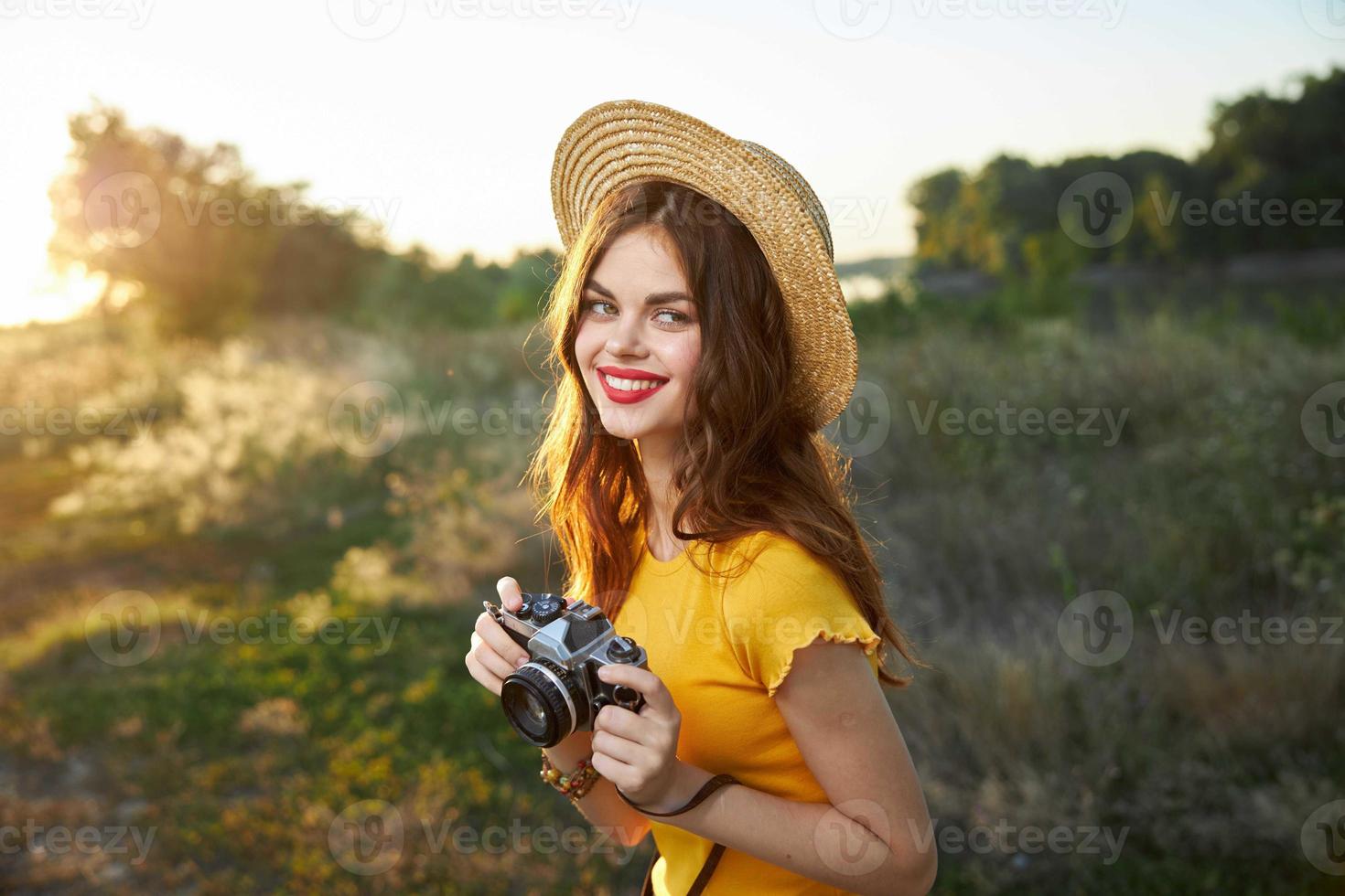 mulher fotógrafo com uma Câmera dentro dela mãos sorrir vermelho lábios chapéu amarelo camiseta verão natureza foto