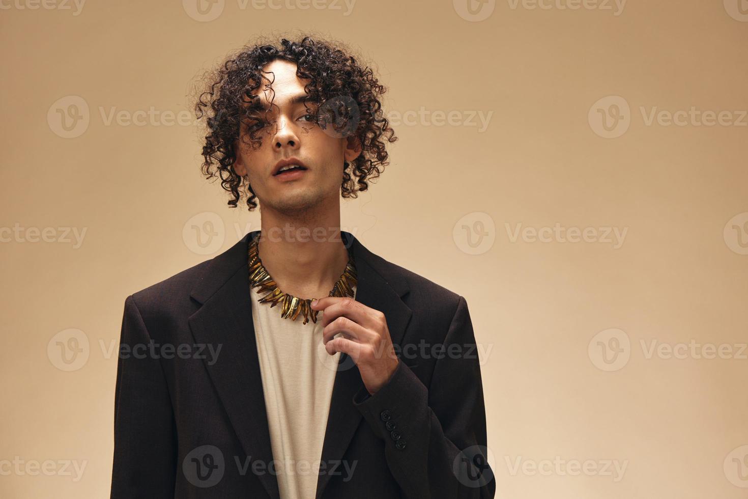 impressionante bronzeada encaracolado homem dentro clássico Castanho Jaqueta toques étnico colar posando isolado em sobre bege pastel fundo. moda Novo coleção oferecer. retro estilo conceito. livre Lugar, colocar para de Anúncios foto