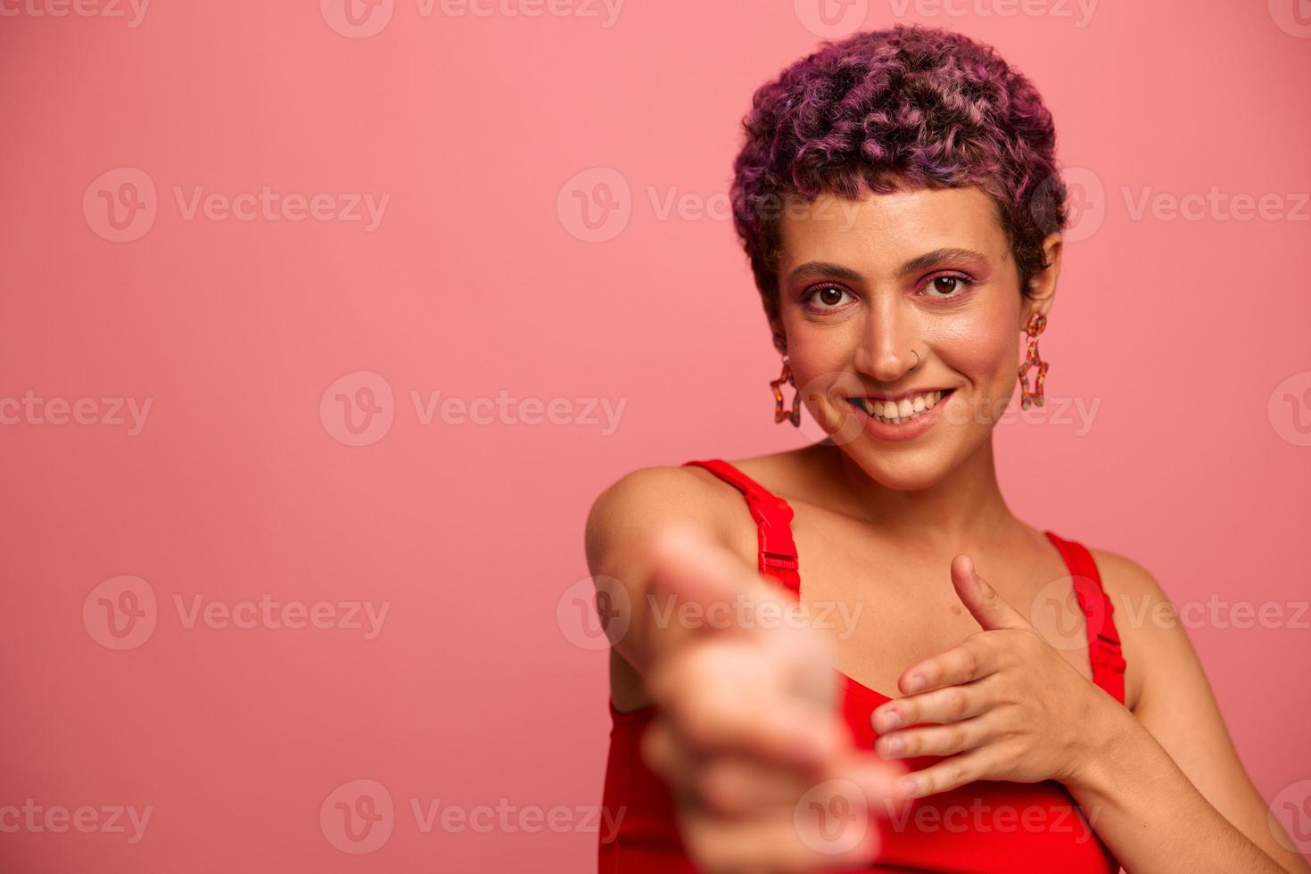 moda retrato do uma mulher com uma curto corte de cabelo do roxa cor e uma sorrir com dentes dentro uma vermelho topo em uma Rosa fundo dançando alegremente foto