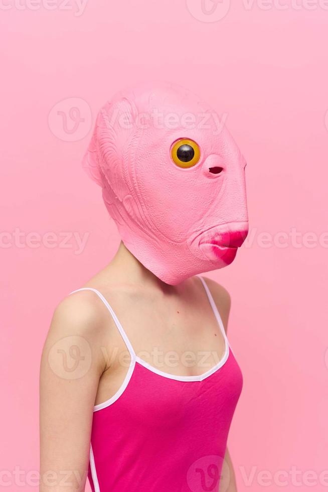 engraçado louco mulher em uma Rosa fundo em pé dentro uma peixe cabeça mascarar em uma Rosa fundo, conceptual dia das Bruxas traje arte foto