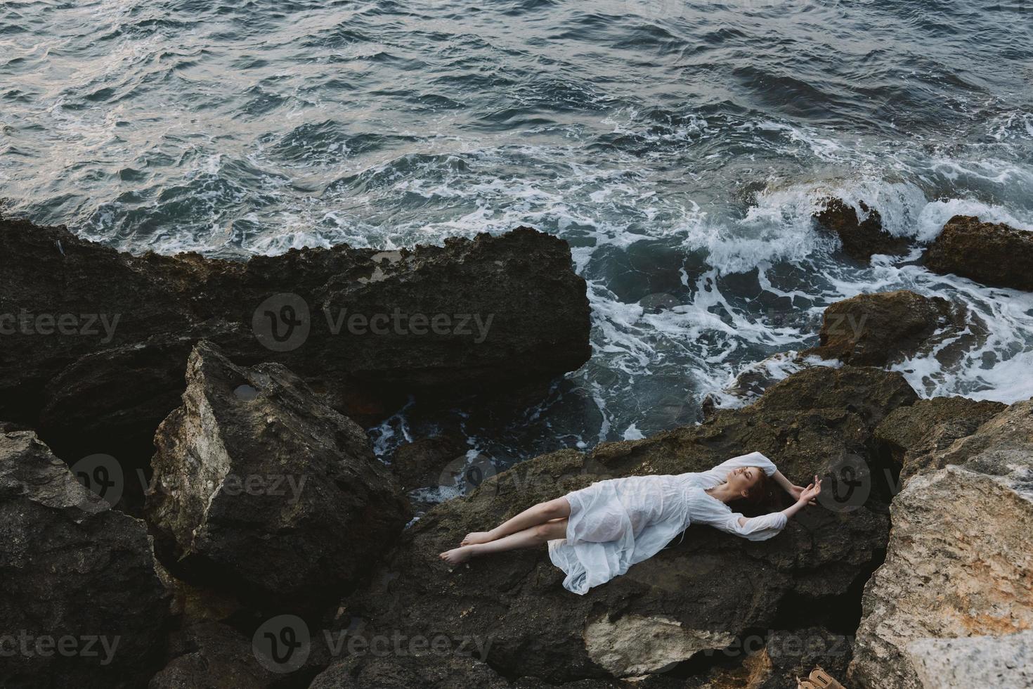 descalço mulher dentro uma isolado local em uma selvagem rochoso costa dentro uma branco vestir Visão a partir de acima foto