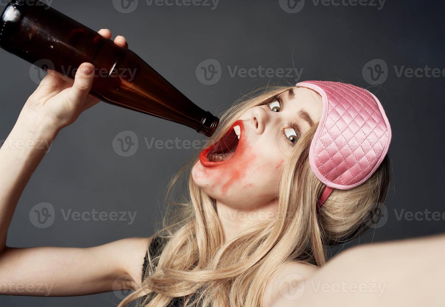 bêbado Loiras menina com uma garrafa do Cerveja gestos com dela mãos e uma brilhante Maquiagem vício modelo foto