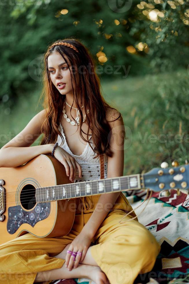 feliz hippie mulher com uma guitarra sorrisos sentado dentro natureza de a lago foto