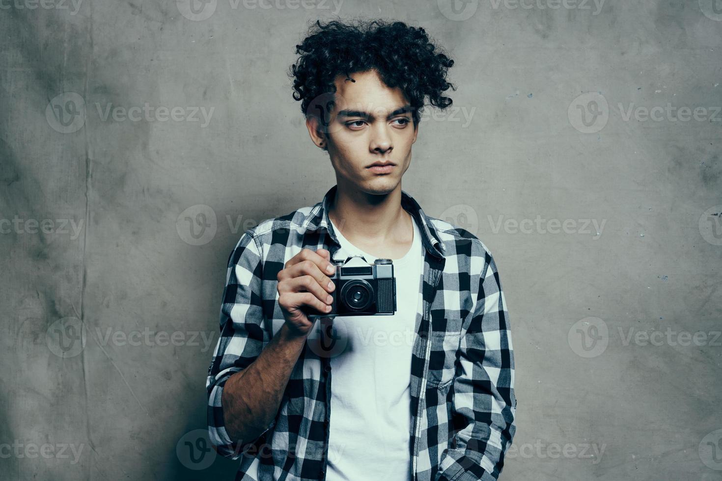 agradável cara dentro uma xadrez camisa e uma camiseta com uma Câmera dentro dele mão modelo passatempo estúdio foto