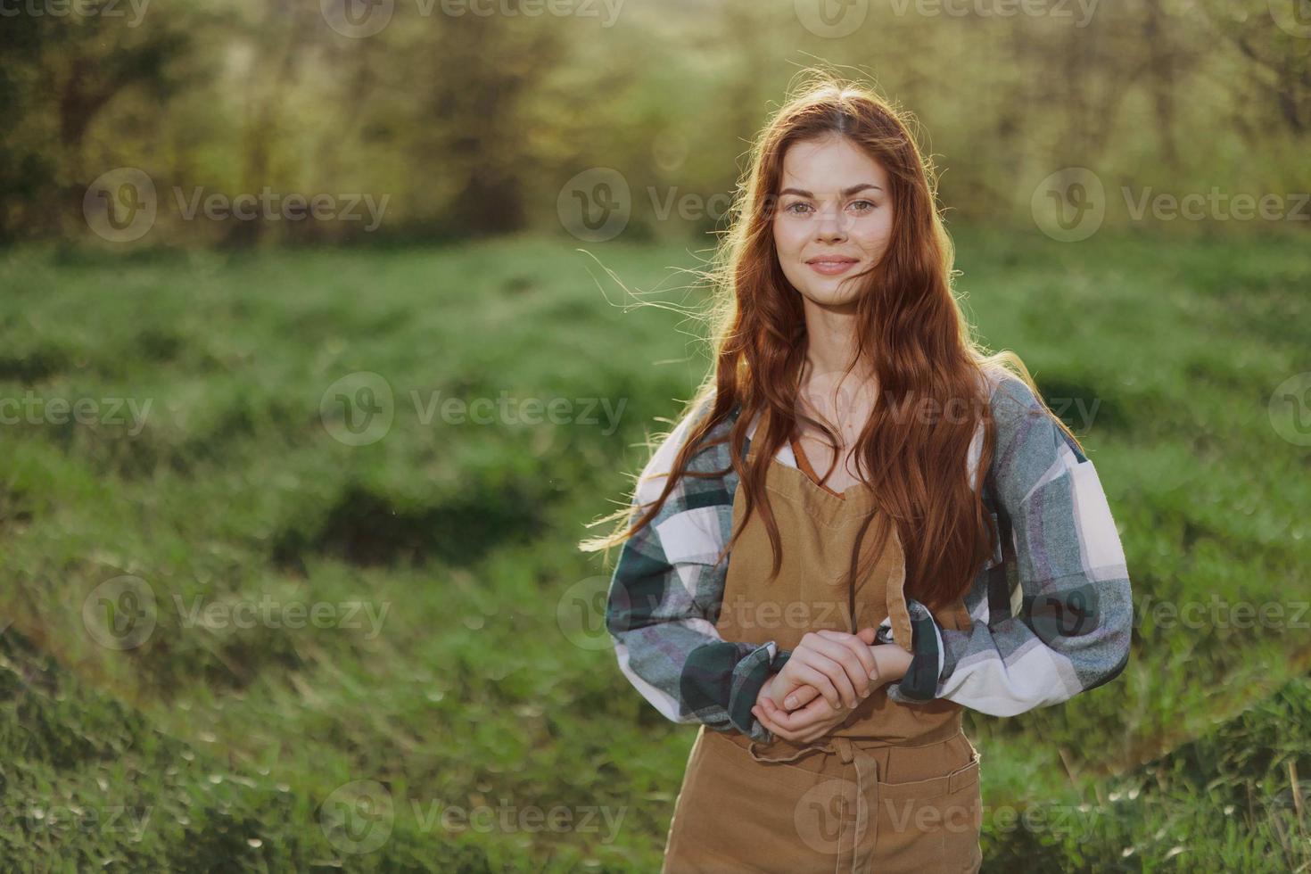 uma mulher jardineiro dentro a avental carrinhos dentro uma campo do verde Relva ao ar livre, sorridente em uma verão tarde para dentro uma ensolarado pôr do sol depois de uma dias trabalhos foto