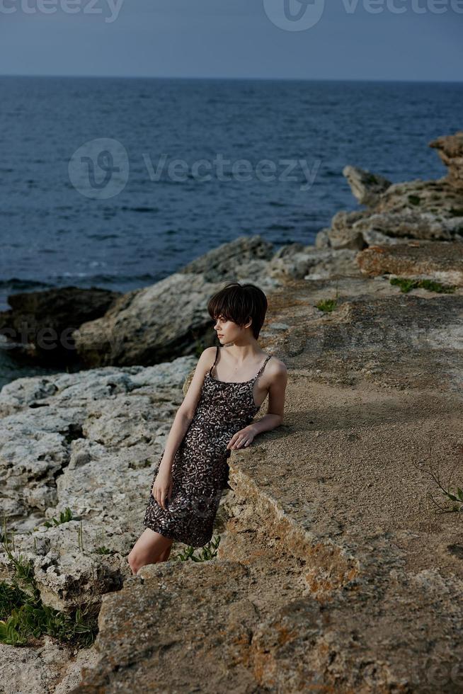 mulher dentro uma brilhante vestir carrinhos em a pedra costa do a oceano natureza inalterado foto