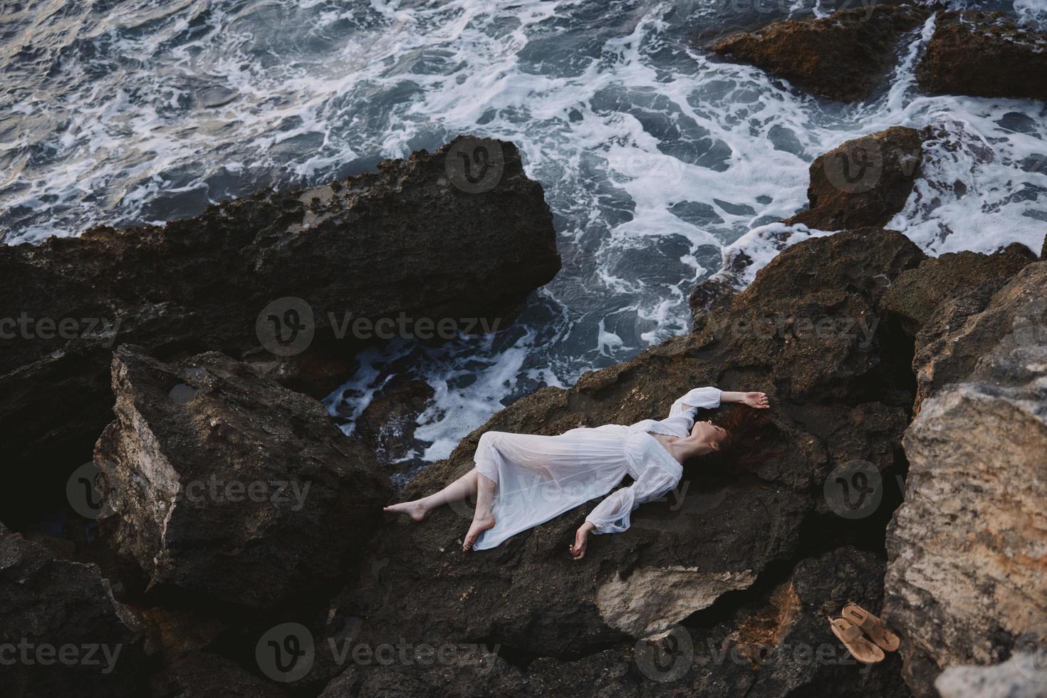 lindo jovem mulher deitado em dela costas em uma rochoso Beira Mar inalterado foto