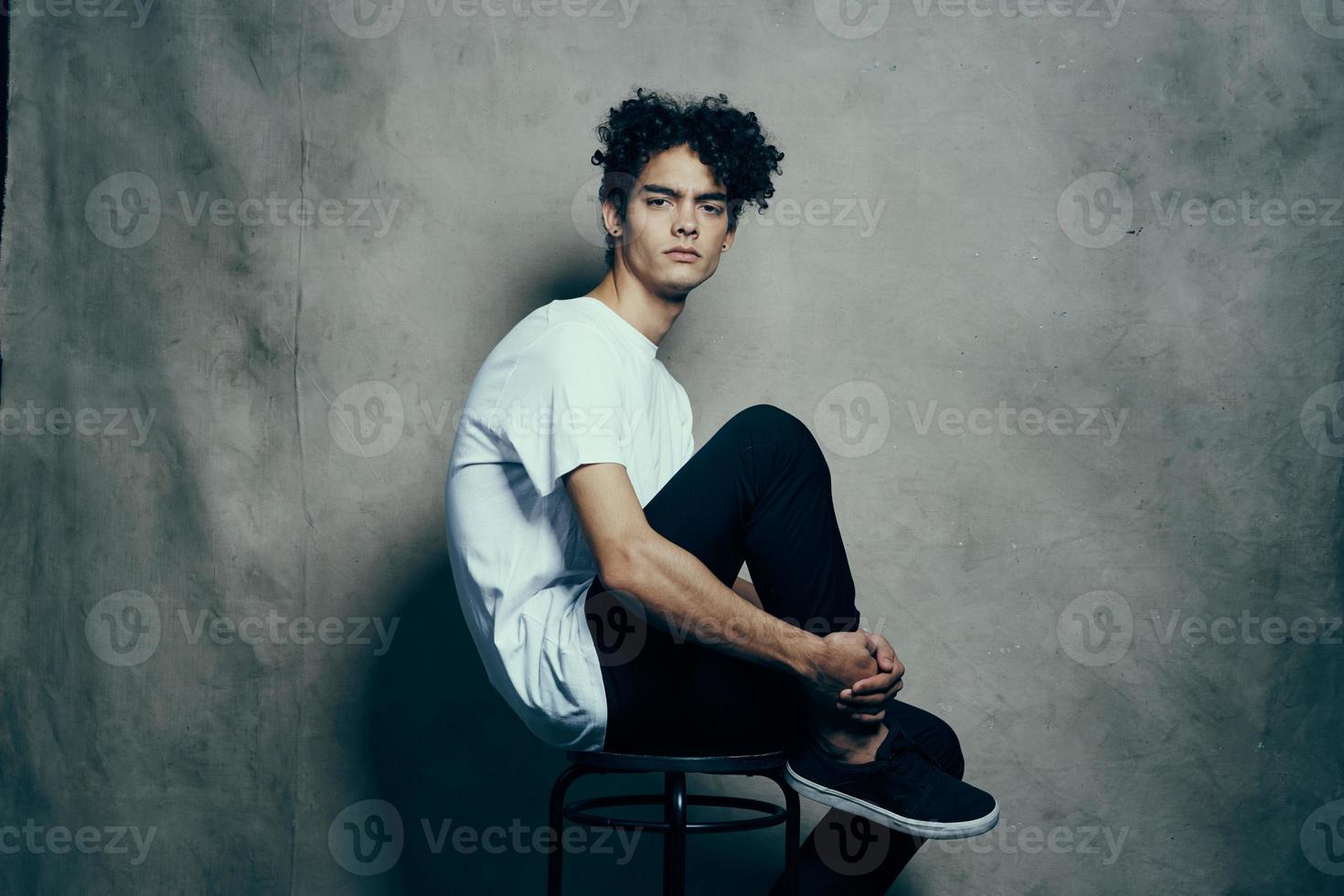 fofa cara com encaracolado cabelo sentado em uma cadeira estúdio foto