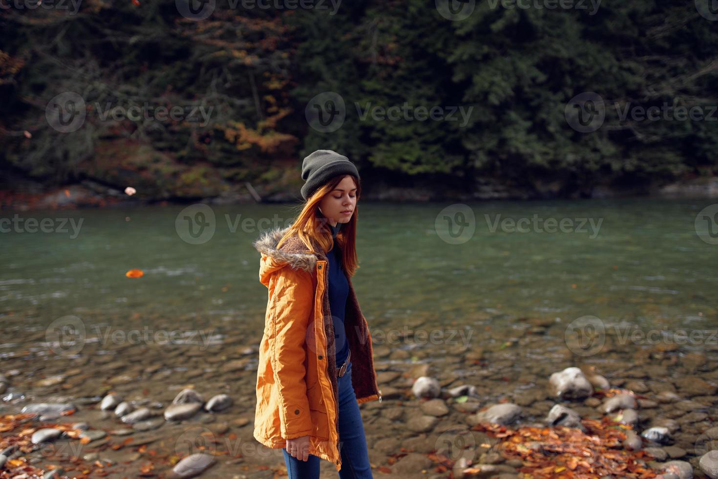 mulher dentro uma amarelo Jaqueta perto a rio admira natureza outono floresta foto