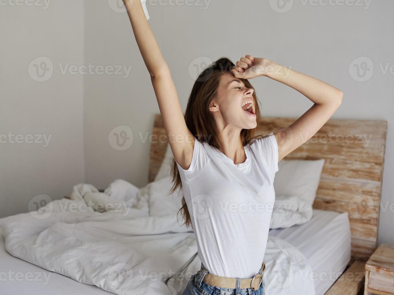 feliz mulher gesticulando com mãos e sentado em cama dentro de casa cortada Visão foto