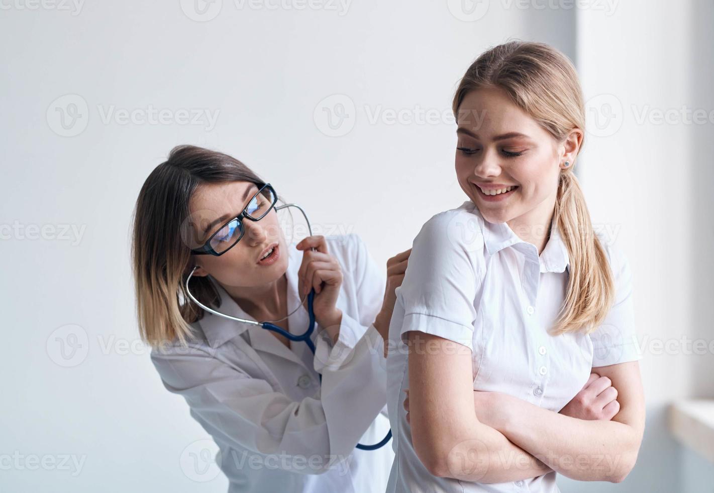 feliz mulher médico examinar fêmea paciente dentro branco camiseta saúde modelo foto