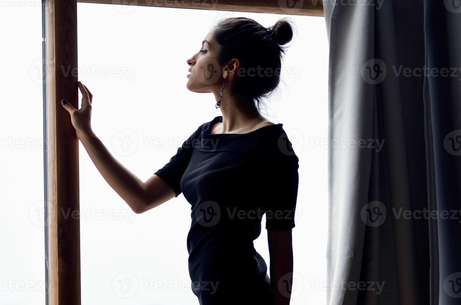 lindo mulher dentro uma Preto vestir perto a janela posando elegante estilo foto