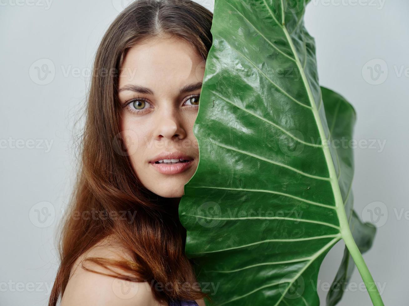 mulher segurando uma ampla verde folha perto dela face atraente Visão cortada Visão do a trópicos foto