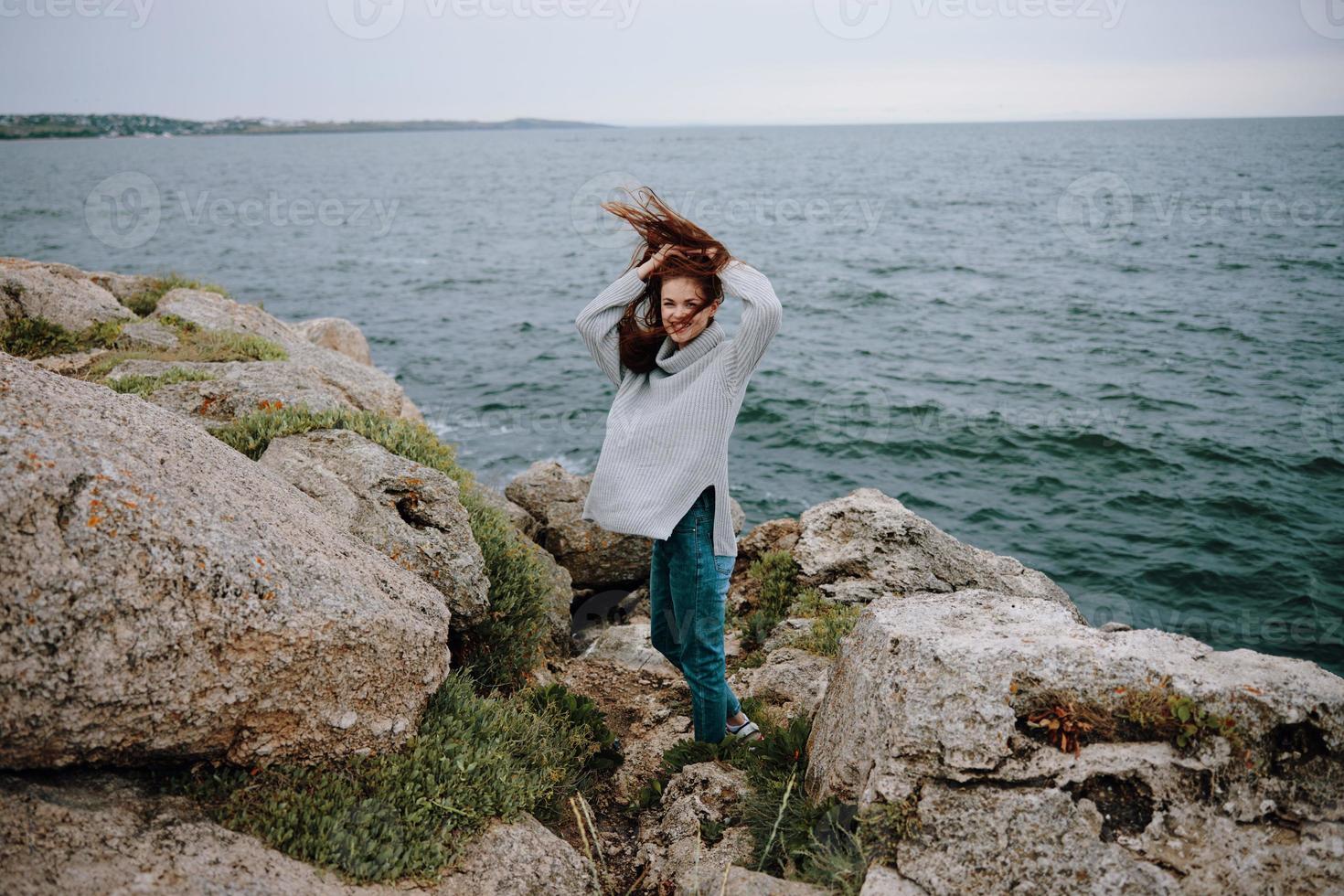 bonita mulher dentro uma cinzento suéter carrinhos em uma rochoso costa natureza inalterado foto