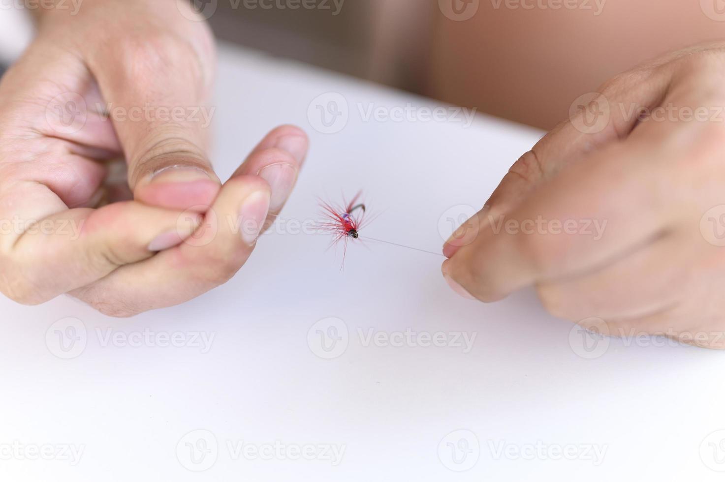 mãos de homem amarrando uma linha de pesca com uma mosca em um anzol foto